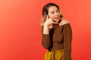 Portrait of young pretty woman in brown casual blouse smiling, showing a gesture of a phone and...