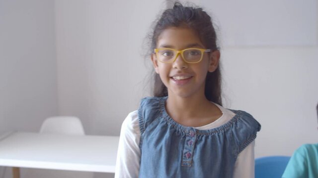 Pretty Latin school girl wearing glasses, standing in classroom and looking at camera. Child portrait concept