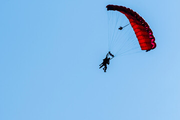 Tandem parachute jump. Silhouette of skydiver flying in blue clear sky