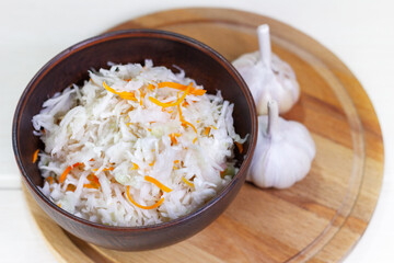 Sauerkraut with carrots in bowl on wooden background. Marinated vegetables.