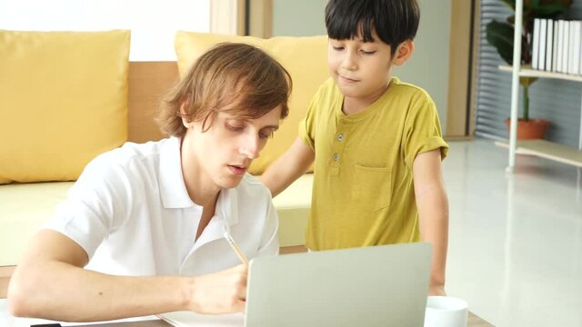 young caucasian white shirt woking on laptop notebook computer with son playing . work from home new normal concept.
