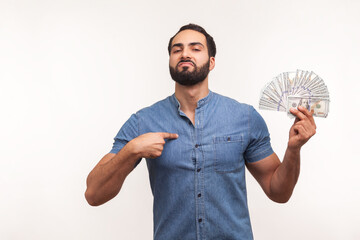 Rich bearded businessman pointing finger at itself and showing many dollar banknotes, proud of his...