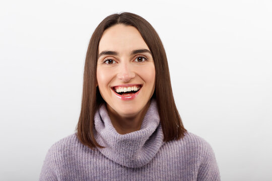 Studio shot of smiling glad woman has appealing appearance, smiles broadly, dressed purple sweater poses against white background expresses positive emotions likes what she sees, rejoices new purchase