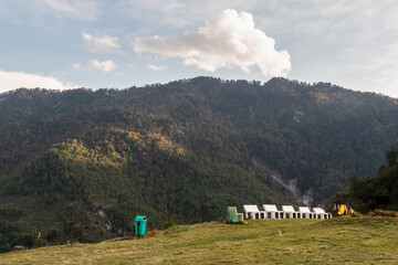 White park benches at the edge of a meadow in a park with mountains behind in the Himalayan village of Munsyari.
