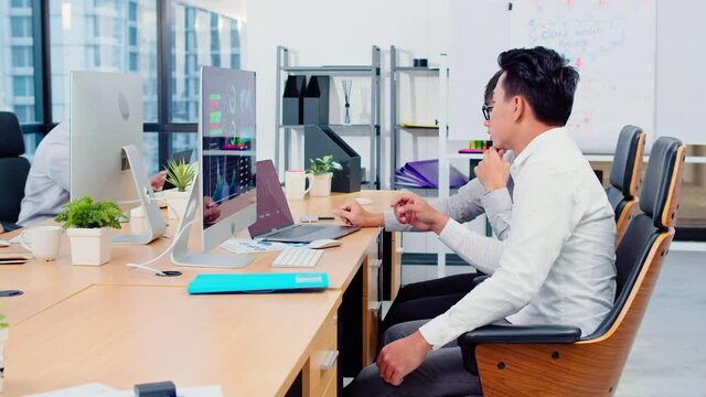 Asian businessman discuss together in office, young coworkers work on laptop and desktop computer. Corporate business, financial consult, partnership teamwork, or information technology concept