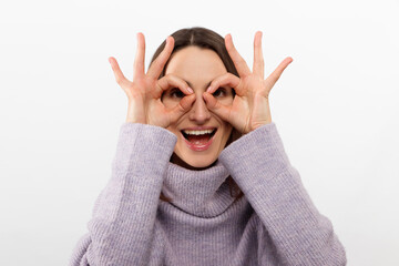 Close up shot of young positive woman with long hair looking at camera through ok-gesture, Beautiful brunette female with dark eyes has playful good mood.