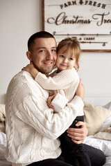 Portrait of a happy loving dad sitting on the bed and hugging his daughter.