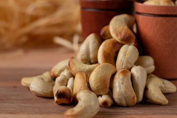 cashew nuts on a wooden table and in two wooden cups with straw background.