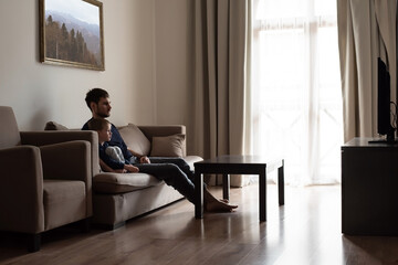 A young father and son are sitting on the sofa, watching TV. Joint leisure of father and son.