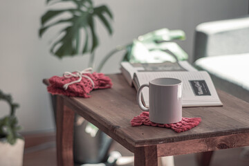 Mesa pequeña, con una taza de café, un libro y portavasos de macramé artesanales