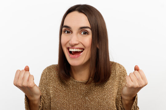 Excited young woman , casual in a golden sweater, screams happily, raises her hands up in surprise, over white studio wall with copy space. Sincere people emotions.