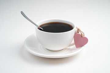 A white coffee Cup and a pink heart tied to the handle of the Cup on a light background. Side view with space for copying. Concept of holiday backgrounds.