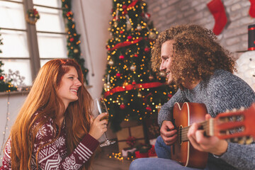 Couple playing the guitar, singing Christmas songs and drinking wine