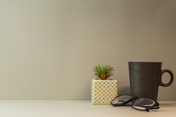 Escritorio de fondo gris con taza de café, planta decorativa y gafas de lectura