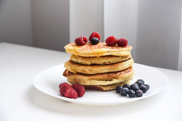A plate of pancakes with honey and fruit. Delicious American pancakes with honey, blueberries and raspberries on the kitchen table.