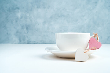 Two hearts are tied to the handle of a coffee Cup on a blue and white background. Side view with space for copying. Concept of holiday backgrounds.