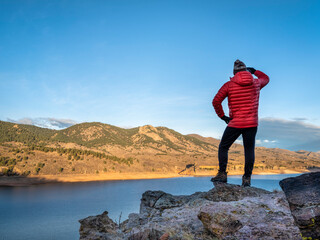 Obraz premium male hiker in a down jacket on a cliff overlooking Horsetooth Reservoir, popular recreation destination for boating, hiking and biking in northern Colorado, fall scenery at sunrise