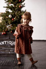 Stylish little girl runs around an artificial decorative Christmas tree in a bright room.