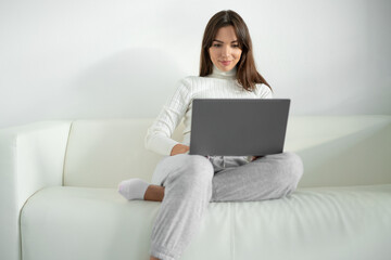 Fototapeta na wymiar Young woman sitting on sofa and using laptop for work.