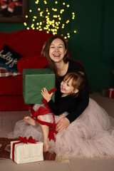 Portrait of a young mother with her little daughter having fun and opening Christmas presents.