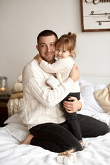 Portrait of a happy loving dad sitting on the bed and hugging his daughter.