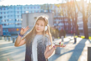 Smiling young girl in headphones listens to music from the phone