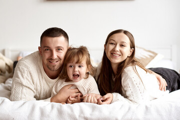 Portrait of a young happy family lying in bed smiling and looking at the camera.