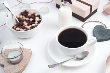 A Cup of coffee and a plate with wheat balls on a festive background with hearts and a gift on a light background. Top view with space to copy. The concept of Valentine's day.
