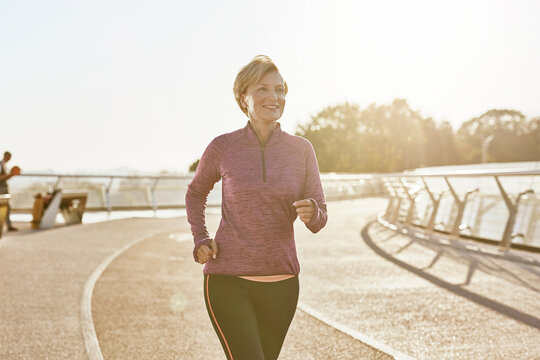 Improving health. Portrait of happy motivated mature woman in sportswear running outdoors on a sunny day