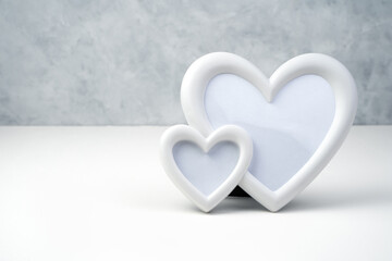 Background for Valentine's day from a white frame in the shape of two hearts on a white-gray background. Side view with space for copying. Concept of holiday backgrounds.