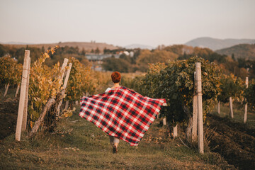 Young woman wrapped in red blanket enjoying sunset at the vineyard.