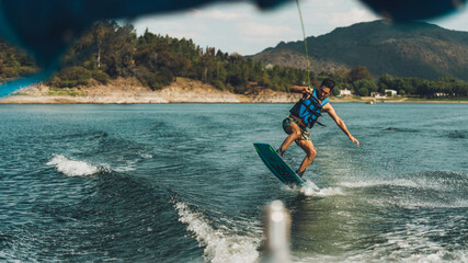 young man doing wakeboarding in a lake whit mountains also doing jumps