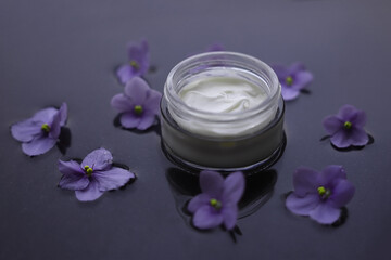 white jar with cream on a background with water decorated with violets