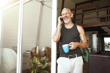 Good news. Happy middle aged caucasian man talking by mobile phone while drinking coffee near balcony of his modern flat