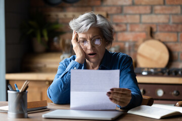Unhappy mature wearing glasses reading bad news in letter, stressed grey haired female with open...