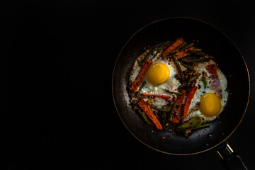 Two fried eggs in a pan with large slices of carrots, bell pepper and asparagus with spices and sauce.