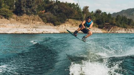 Fototapeta premium young man doing wakeboarding in a lake whit mountains also doing jumps