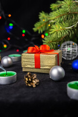Golden present gift box with red ribbon next to the christmas tree, candles and holiday decoration. Merry Christmas or Happy New Year greeting card.