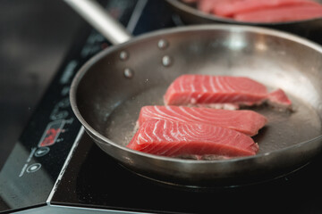 Two frying pans with tuna steak on induction stove