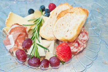top, front view, close distance of a plate of sliced salami, variety of cheeses, sliced French bread, blueberries, variety of cheese,  food pairings for a French wine tasting event

