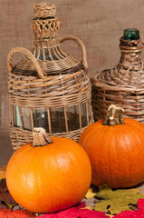 top, front view of two, local, freshly picked pumpkins with wine bottles in wood wicker carriers on a tan burlap tie covering