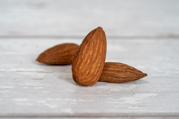 Close-up of three isolated almonds standing up on a white wooden table in a white background. Close-up and minimalist shot with copy space for text