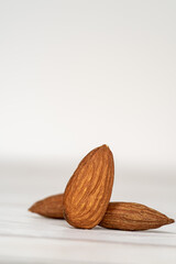 Close-up of three isolated almonds standing up on a white wooden table in a white background. Close-up and minimalist shot with copy space for text