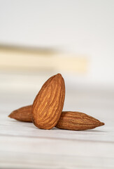 Close-up of three isolated almonds standing up on a white wooden table in a white background. Close-up and minimalist shot with copy space for text