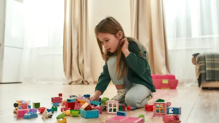 Fotobehang Lego A cute little girl playing with her toys on the floor of a spacy kitchen  © Svitlana