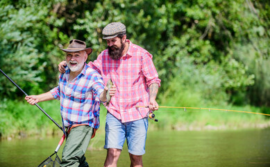 Sunny summer day at river. Fisherman family. Hobby sport. Fishing peaceful activity. Father and son fishing. Rod tackle. Fishing equipment. Grandpa and mature man friends. Fishing with spinning reel