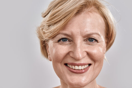 Close up shot of face of beautiful middle aged woman smiling at camera while posing isolated against grey background