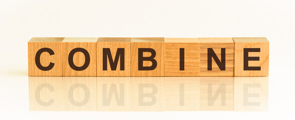 Wooden Blocks with the text: combine. The text is written in black letters and is reflected in the mirror surface of the table.