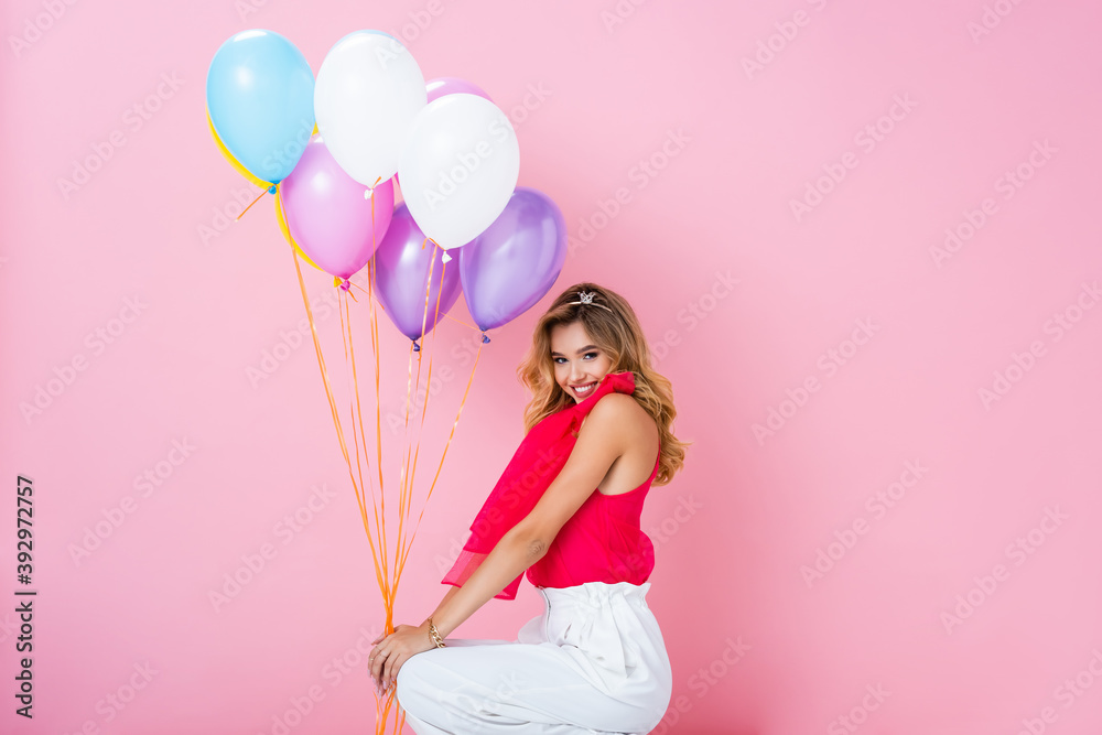 Wall mural elegant happy woman in crown with balloons on pink background