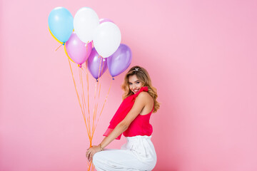 elegant happy woman in crown with balloons on pink background